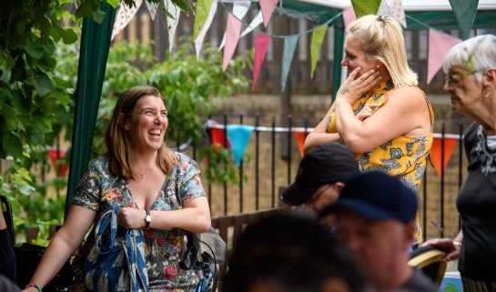 Two people sit outside with bunting, smiling together. (c) Alex Brennan